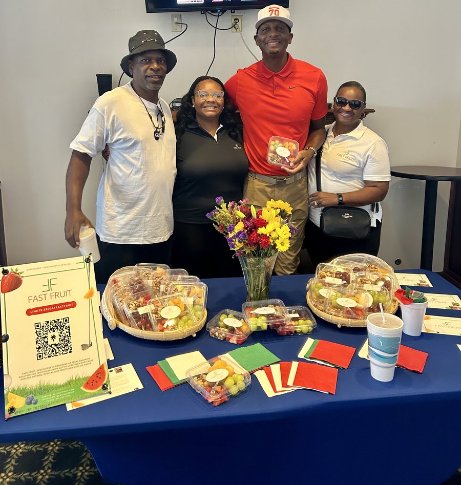 Fast Fruit team members standing behind a branded community event table with packaged fruit containers, flowers, and informational materials.
